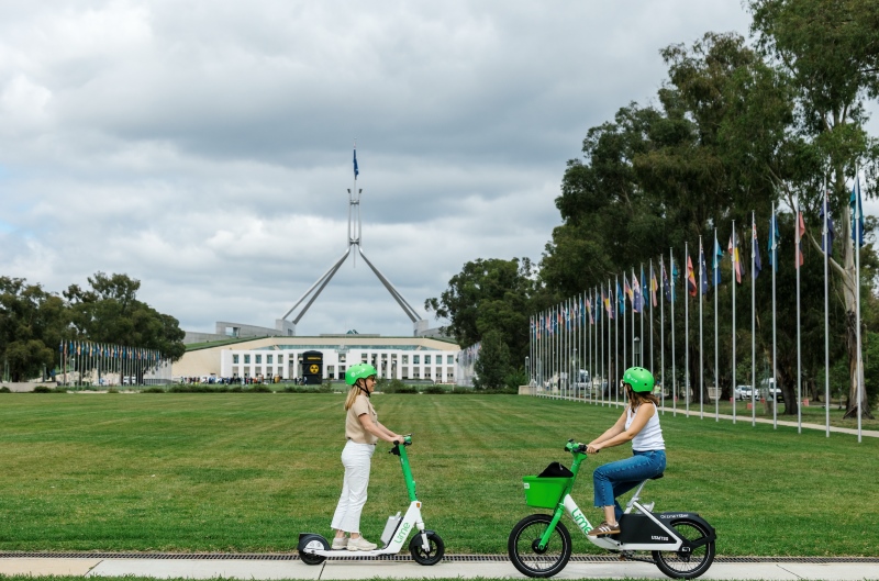 E-scooter and e-bike riders passing each other with background to parliament house Canberra