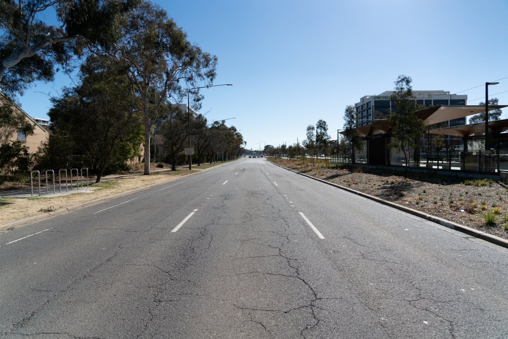Image of 3 lane road with faded white line markings and cracked pavement. 