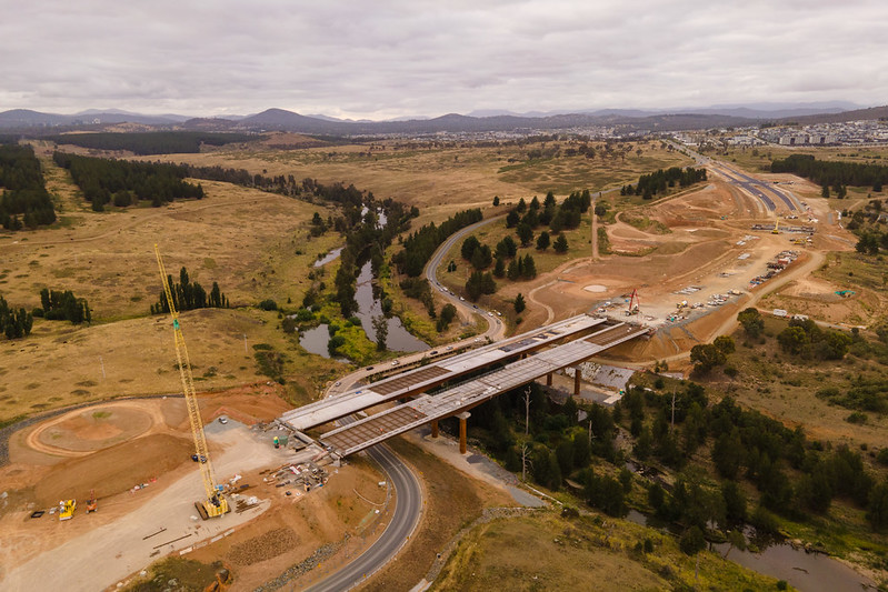 A bridge being constructed over a river running through green hills.